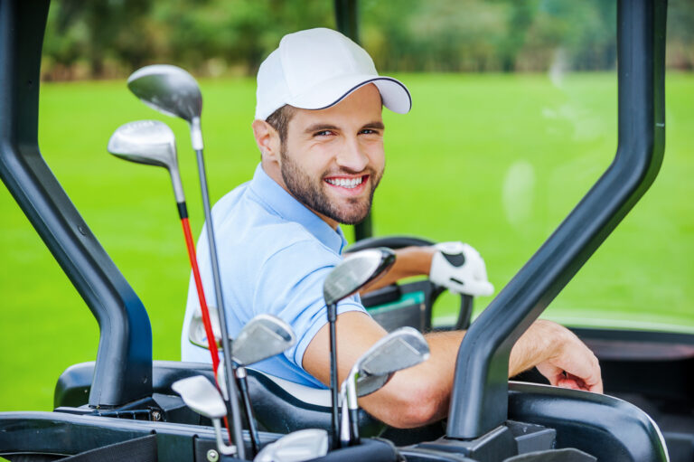 Golfer in golf cart. Rear view of young happy male golfer driving a golf cart and looking over shoulder
